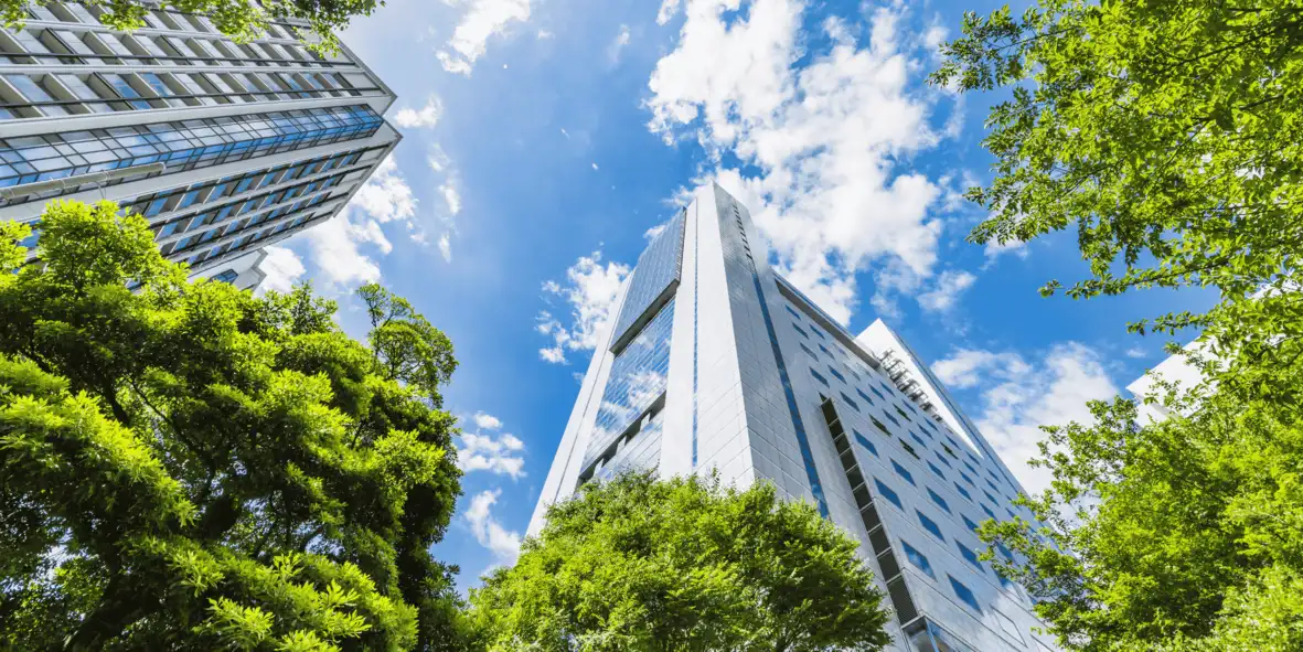 Modern high-rise buildings surrounded by lush green trees under a blue sky, symbolising the integration of biodiversity in sustainable urban development.